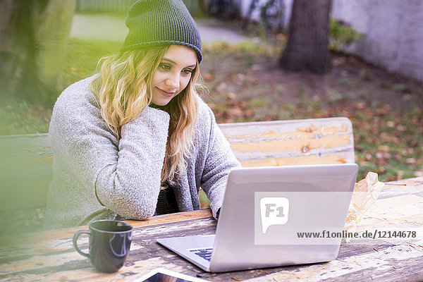 Porträt einer lächelnden jungen Frau mit Laptop-Skyping im Herbst im Freien