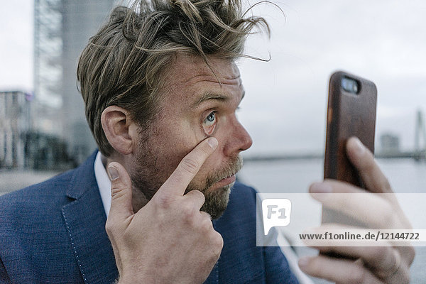 Businessman with cell phone examining his eye