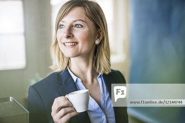 Lächelnde Geschäftsfrau mit Espressotasse im Büro