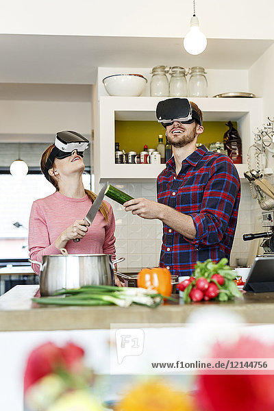 Happy young couple wearing VR glasses cooking together in kitchen