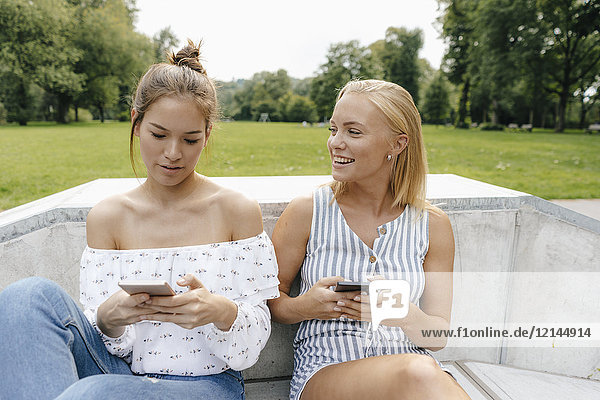 Zwei glückliche junge Frauen mit Handys im Skatepark