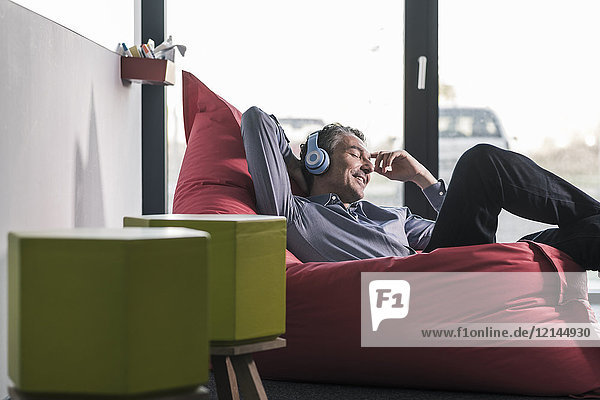Smiling businessman sitting in beanbag wearing headphones