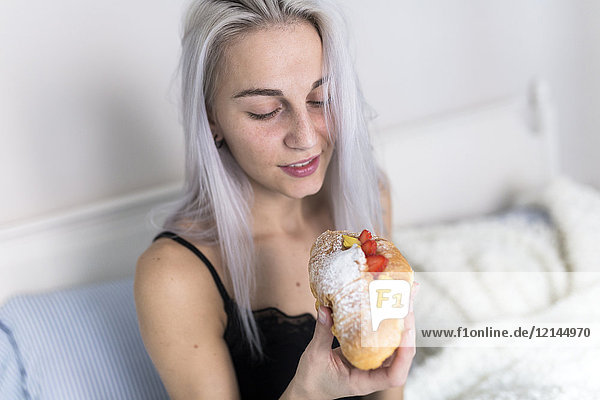 Junge Frau genießt ein süßes Croissant im Bett