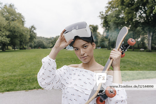 Portrait einer jungen Frau mit VR-Brille  die Skateboard hält