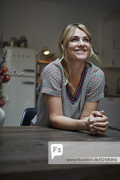 Porträt einer glücklichen Frau  die sich auf den Küchentisch lehnt.