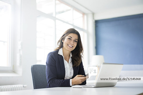 Porträt einer glücklichen Geschäftsfrau am Schreibtisch im Büro