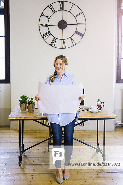 Smiling woman in home office holding blueprint