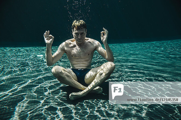 Mann sitzt in Yoga-Pose unter Wasser in einem Schwimmbad
