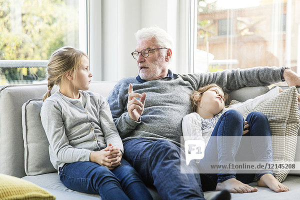 Großvater im Gespräch mit zwei Mädchen auf dem Sofa im Wohnzimmer