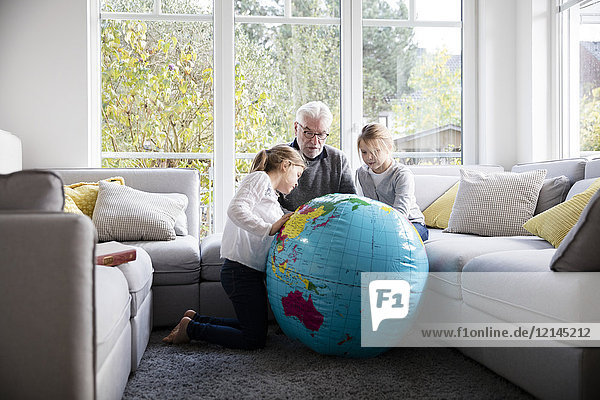Zwei Mädchen und Großvater mit Globus im Wohnzimmer