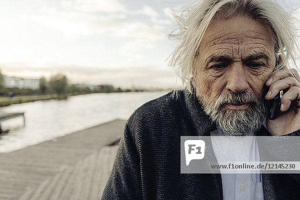 Porträt eines ernsthaften älteren Mannes auf dem Handy am See