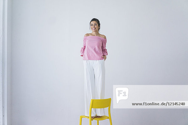 Porträt der lachenden Frau auf gelbem Stuhl stehend