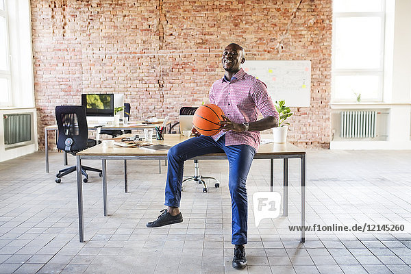 Happy businessman with basketball at desk in office