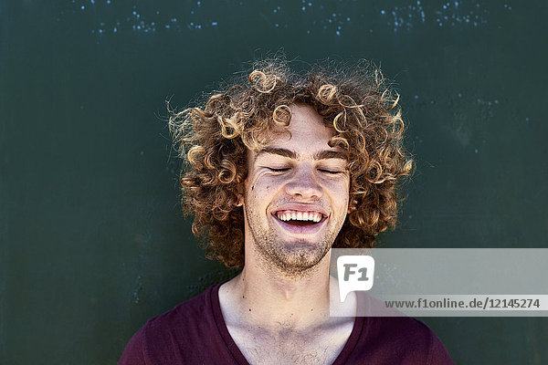 Porträt eines lachenden jungen Mannes mit lockigen Haaren vor einer grünen Wand