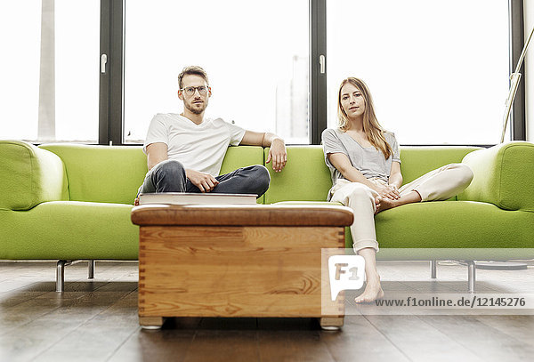 Porträt eines seriösen jungen Paares  das zu Hause auf der Couch sitzt.