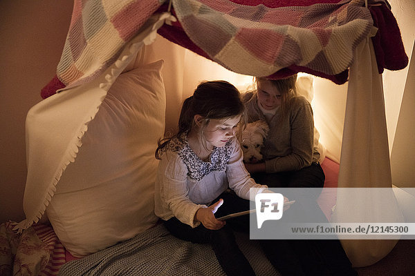 Two girls with dog and tablet in children's room