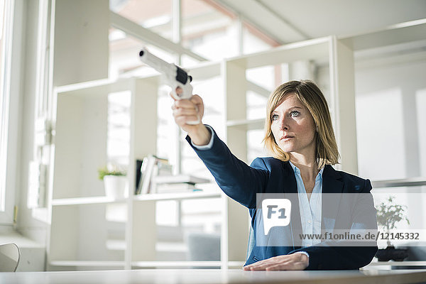 Businesswoman aiming with gun in office