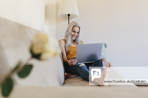 Smiling young woman using laptop on couch at home