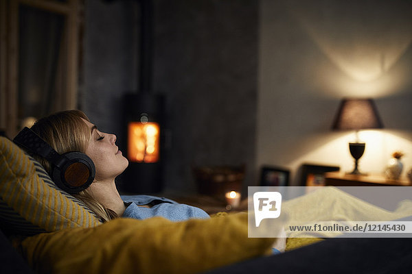Lächelnde Frau beim Musikhören mit Kopfhörern auf der Couch zu Hause am Abend