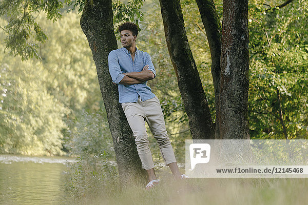 Young man in park leaning against a tree at the water