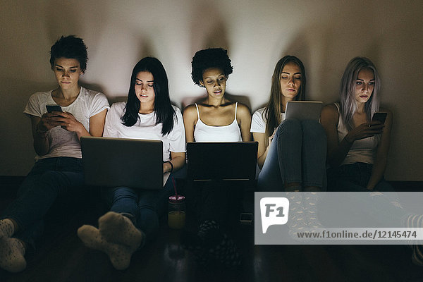 Group of female friends at home sitting on floor using technology in the dark