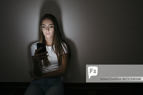 Young woman at home sitting on floor using cell phone in the dark