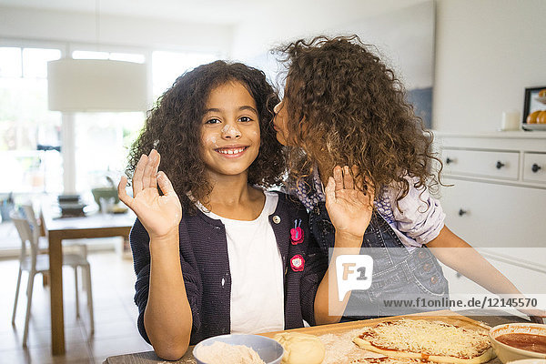 Little girl kissing sister in kitchen  baking pizza