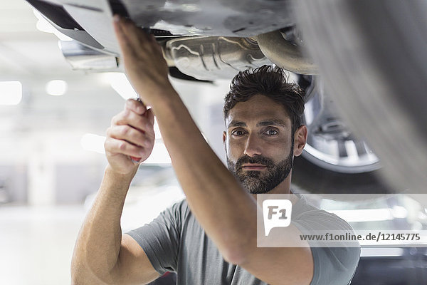 Porträt eines seriösen Mechanikers, der unter dem Auto in einer Autowerkstatt arbeitet.