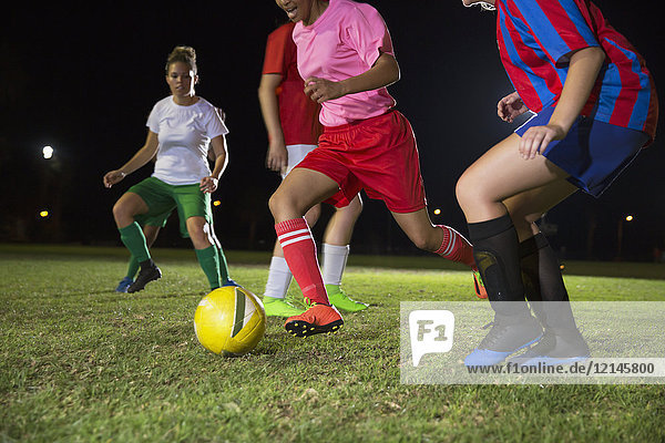Junge Fußballspielerinnen,  die nachts auf dem Spielfeld spielen und um den Ball rennen.