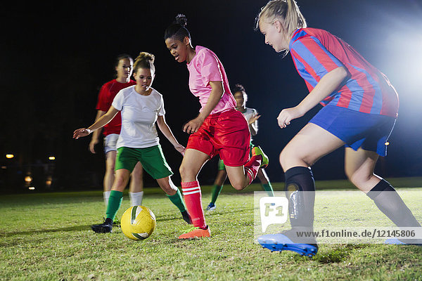 Young female soccer players playing on field at night  running for ball