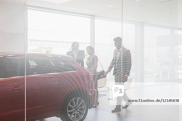 Autoverkäufer zeigt Neuwagen den Kunden im Autohaus-Showroom