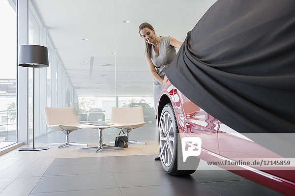 Autoverkäuferin beim Entfernen des Deckels von Neuwagen im Autohaus-Showroom