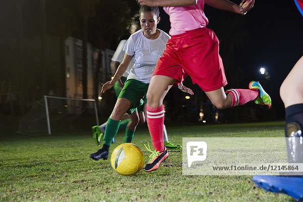 Junge Fußballspielerinnen  die nachts auf dem Spielfeld spielen und den Ball treten.