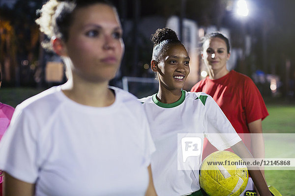 Smiling  confident young female soccer players on field at night