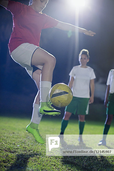 Junge Fußballspielerin übt, springt und tritt den Ball nachts auf dem Spielfeld.