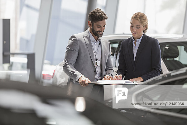 Autoverkäufer und Kundin bei der Überprüfung der finanziellen Vertragsunterlagen im Autohaus-Showroom