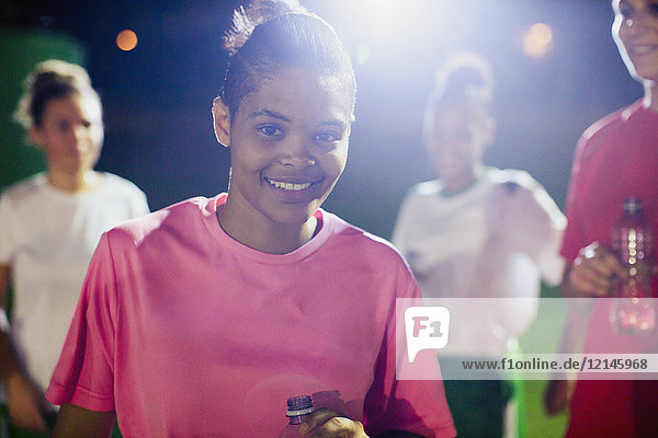 Portrait confident young female soccer player on field with teammates at night