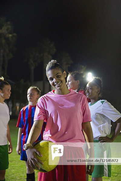 Portrait lächelnde  selbstbewusste junge Fußballspielerin mit Ball auf dem Spielfeld bei Nacht