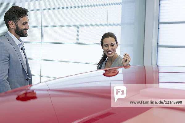 Lächelnder Autoverkäufer zeigt Neuwagen der Kundin im Autohaus-Showroom