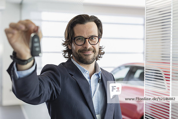 Portrait confident car salesman holding,  showing car key in car dealership showroom