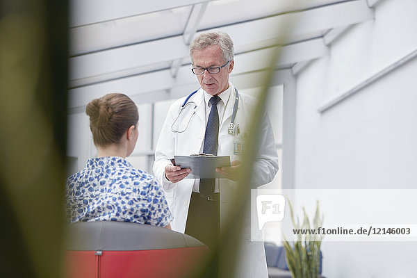 Männlicher Arzt mit Klemmbrett im Gespräch mit Patientin in der Lobby des Krankenhauses