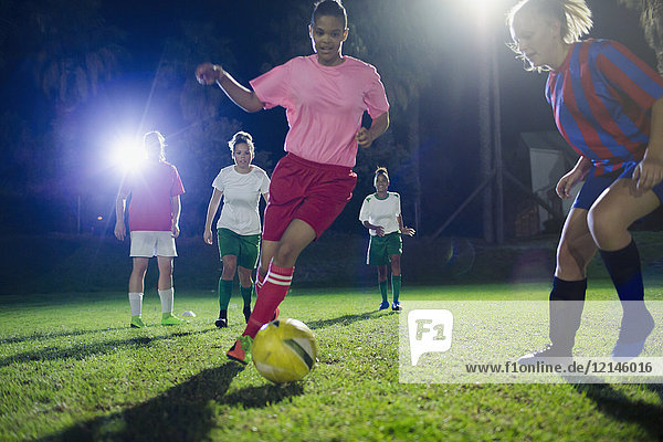 Young female soccer players playing on field at night  kicking the ball