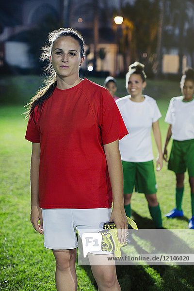 Portrait confident young female soccer player on field at night