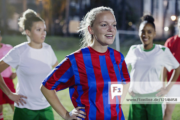 Confident young female soccer players resting with hands on hips on field at night