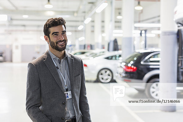Porträt eines lächelnden Autoverkäufers mit Blick in die Autowerkstatt