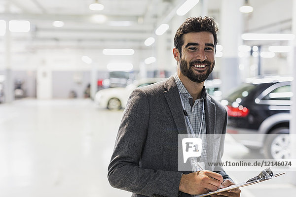 Portrait lächelnder  selbstbewusster Autoverkäufer mit Klemmbrett in der Autowerkstatt