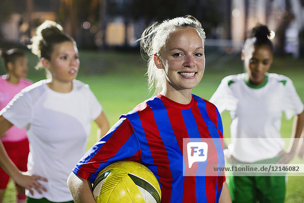 Portrait smiling  confident young female soccer player with ball on field at night