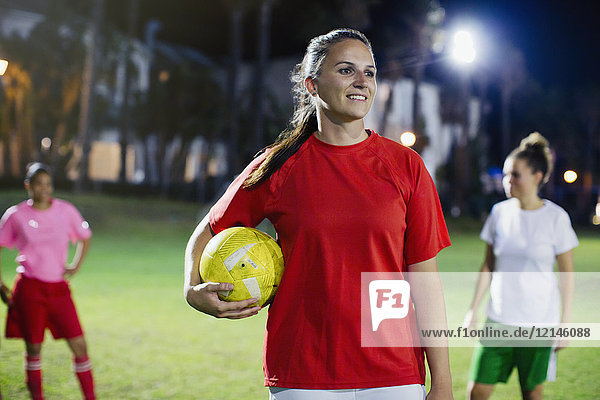 Portrait confident  smiling young female soccer player on field at night