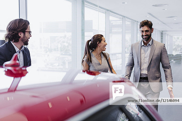 Autoverkäufer und lächelndes Paar Kunden  die sich ein neues Auto im Autohaus anschauen.