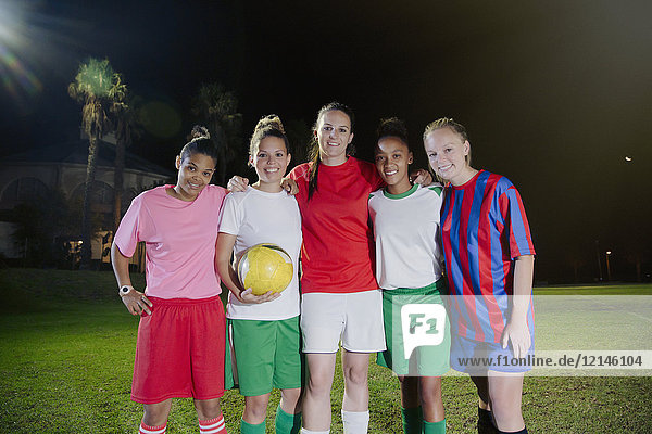 Portrait smiling  confident young female soccer teammates with ball on field at night